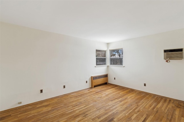 unfurnished room featuring radiator heating unit, light hardwood / wood-style floors, and a wall unit AC