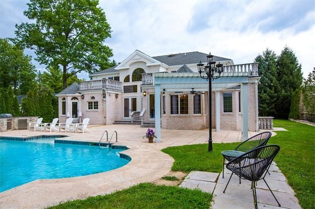 rear view of property featuring ceiling fan, a patio area, a lawn, and a balcony