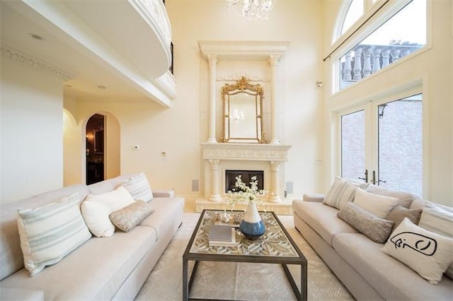 living room with a large fireplace, ornamental molding, a towering ceiling, and an inviting chandelier