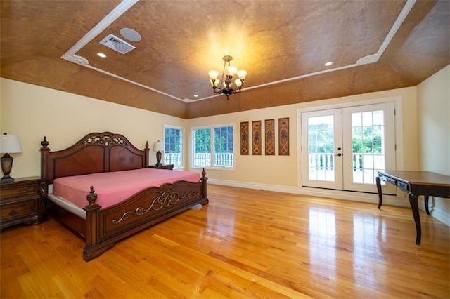 bedroom featuring crown molding, french doors, hardwood / wood-style flooring, a tray ceiling, and a chandelier