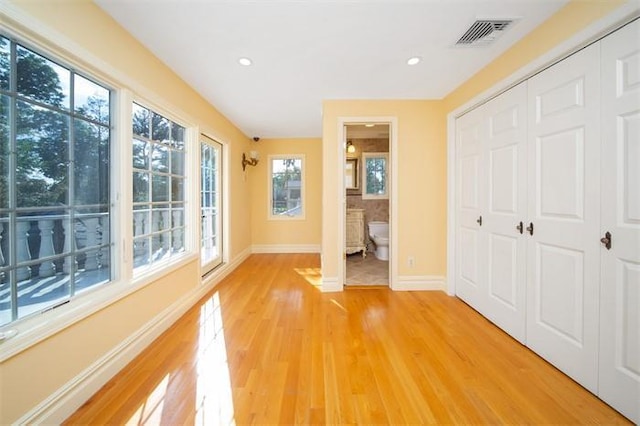 unfurnished bedroom featuring light hardwood / wood-style floors, multiple windows, connected bathroom, and a closet