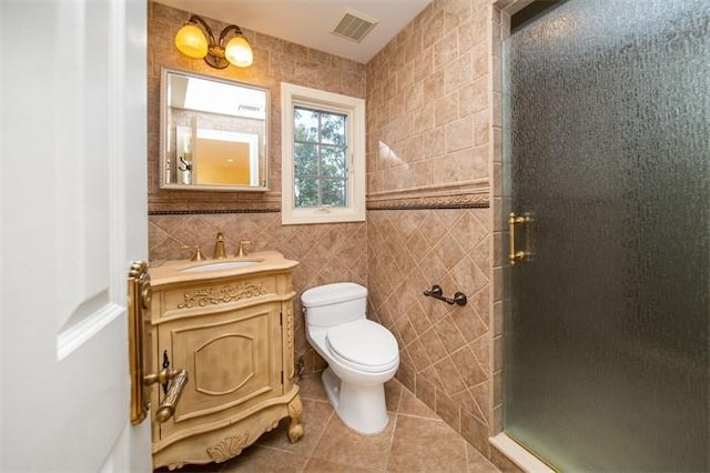 bathroom featuring a shower with door, tile patterned flooring, tile walls, toilet, and vanity