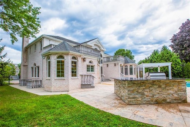 back of property with a balcony, exterior kitchen, a patio area, and a yard