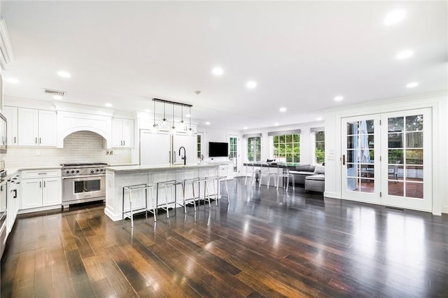 kitchen featuring high end stainless steel range oven, hanging light fixtures, white refrigerator, an island with sink, and white cabinets