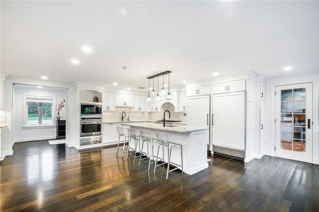 kitchen featuring pendant lighting, built in microwave, white cabinetry, oven, and a center island with sink