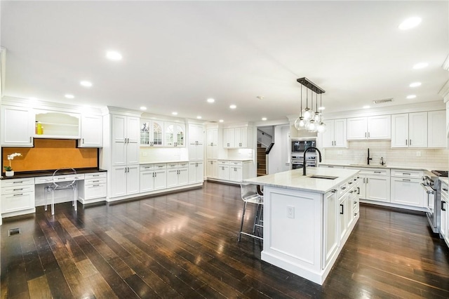 kitchen featuring decorative light fixtures, sink, white cabinets, a kitchen island with sink, and stainless steel appliances