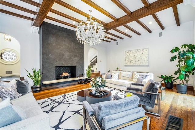 living room featuring hardwood / wood-style flooring, a large fireplace, beam ceiling, and an inviting chandelier