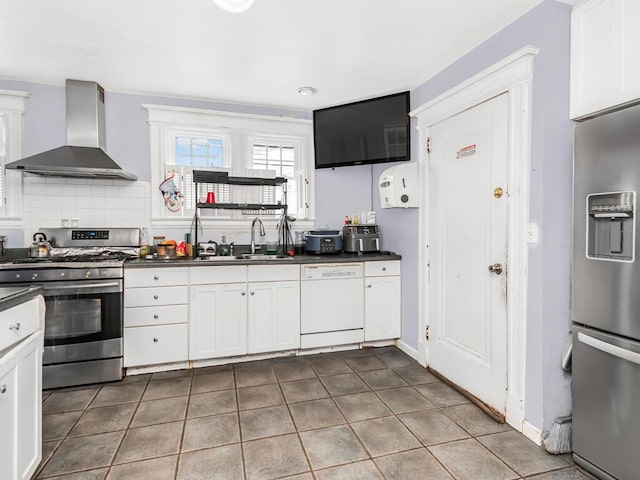 kitchen featuring appliances with stainless steel finishes, tile patterned flooring, wall chimney range hood, white cabinets, and sink