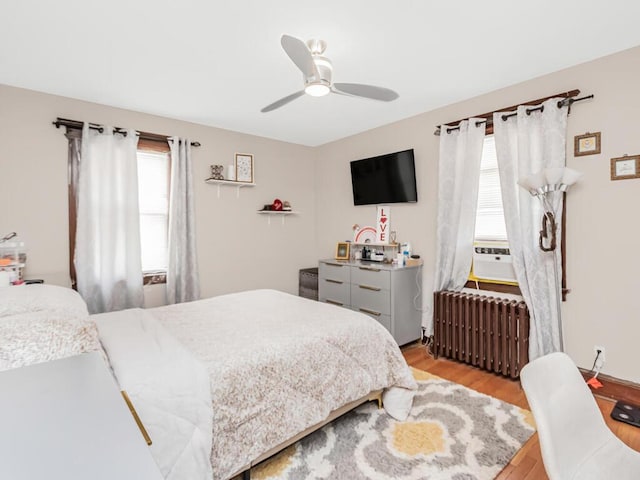 bedroom featuring radiator heating unit, multiple windows, light wood-type flooring, and ceiling fan