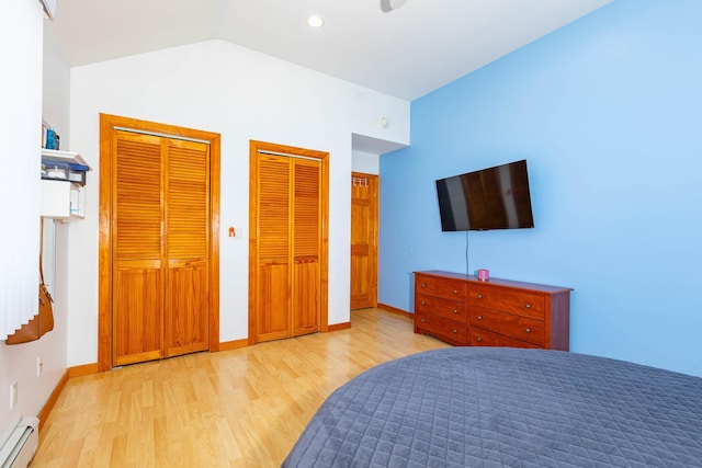 bedroom featuring baseboard heating, light wood-type flooring, vaulted ceiling, and two closets