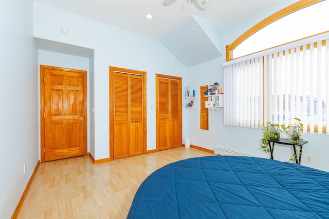 bedroom with light hardwood / wood-style flooring, a baseboard heating unit, two closets, and lofted ceiling