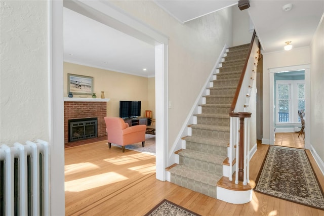 stairs with hardwood / wood-style floors, crown molding, radiator heating unit, and a fireplace