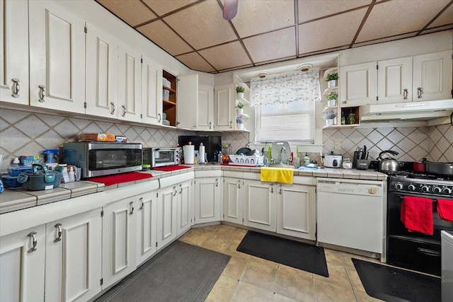 kitchen featuring black range with gas cooktop, white dishwasher, tile counters, white cabinets, and a drop ceiling