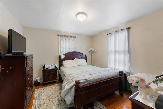 bedroom featuring multiple windows, wood-type flooring, and radiator heating unit