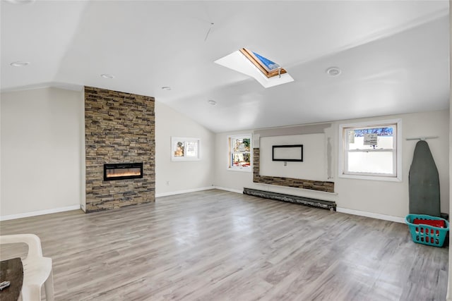 unfurnished living room featuring light wood-type flooring, a baseboard radiator, a fireplace, and vaulted ceiling with skylight