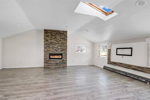 unfurnished living room featuring a baseboard radiator, light hardwood / wood-style flooring, vaulted ceiling with skylight, and a stone fireplace