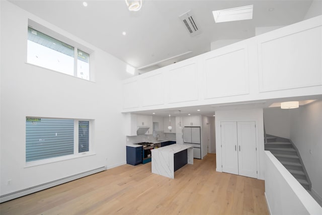 kitchen featuring a baseboard radiator, sink, white cabinetry, a towering ceiling, and light hardwood / wood-style floors