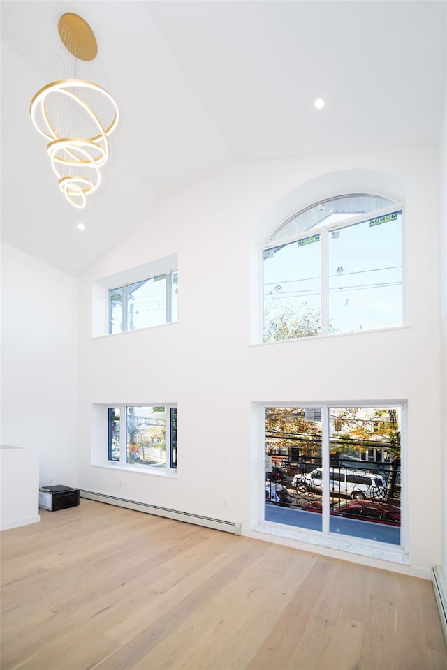 unfurnished living room featuring light hardwood / wood-style floors, a baseboard heating unit, high vaulted ceiling, and a notable chandelier