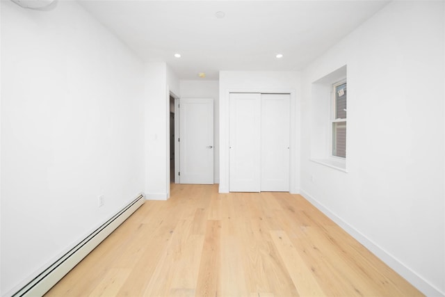 unfurnished bedroom with a baseboard heating unit, light hardwood / wood-style flooring, and a closet