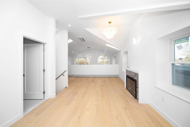 unfurnished living room with light hardwood / wood-style floors, a chandelier, a baseboard radiator, a premium fireplace, and lofted ceiling