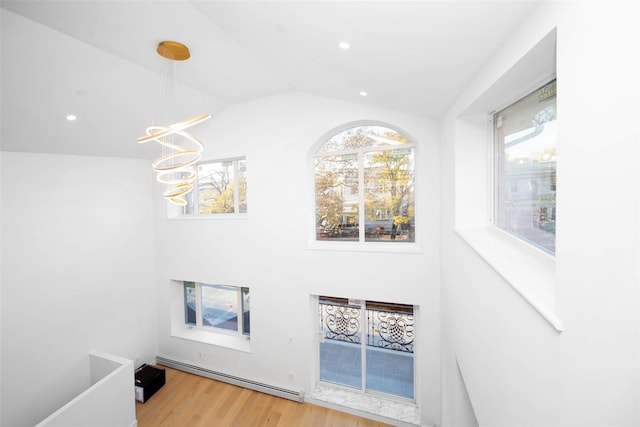 foyer entrance with baseboard heating, wood-type flooring, lofted ceiling, and an inviting chandelier