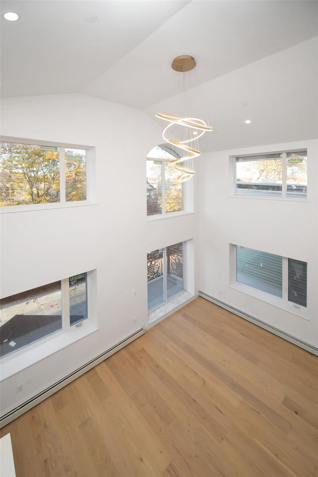 unfurnished living room with a baseboard radiator, hardwood / wood-style flooring, vaulted ceiling, and a notable chandelier