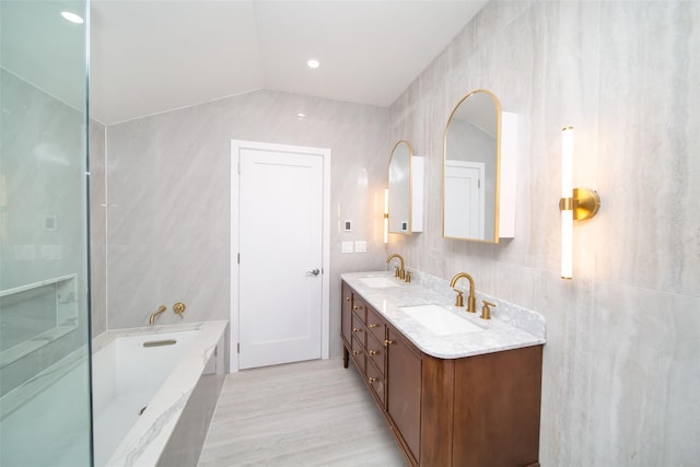 bathroom featuring tile walls, tiled tub, vanity, and vaulted ceiling