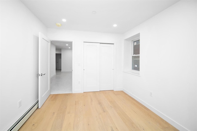 unfurnished bedroom featuring a closet, light wood-type flooring, and baseboard heating