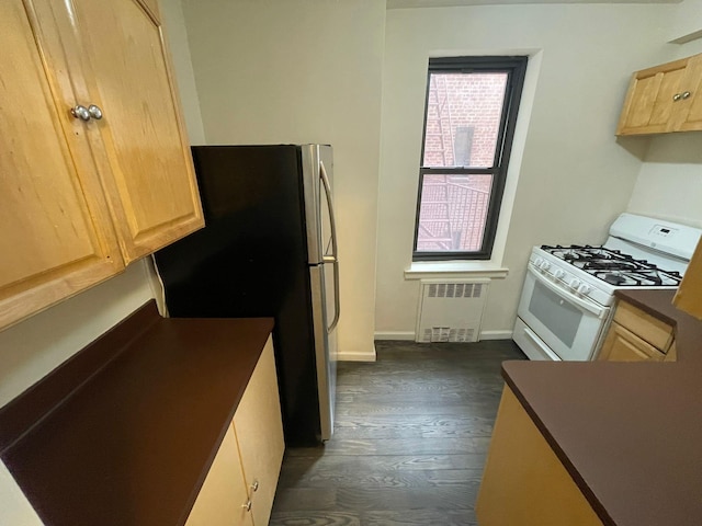 kitchen featuring white gas range oven, radiator heating unit, light brown cabinetry, dark hardwood / wood-style floors, and stainless steel fridge