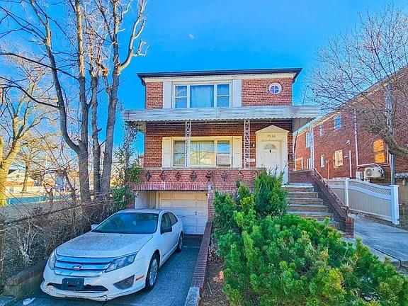 196-64 45th Ave, Flushing, NY 11358 - view of front facade featuring brick siding, a garage, driveway, and fence