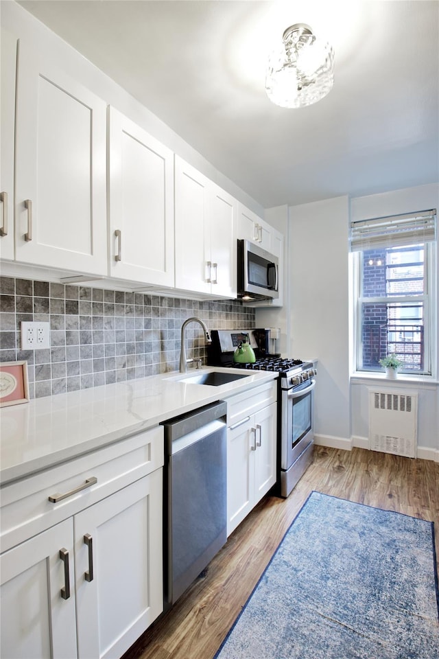 kitchen featuring appliances with stainless steel finishes, radiator, white cabinetry, tasteful backsplash, and light wood-type flooring