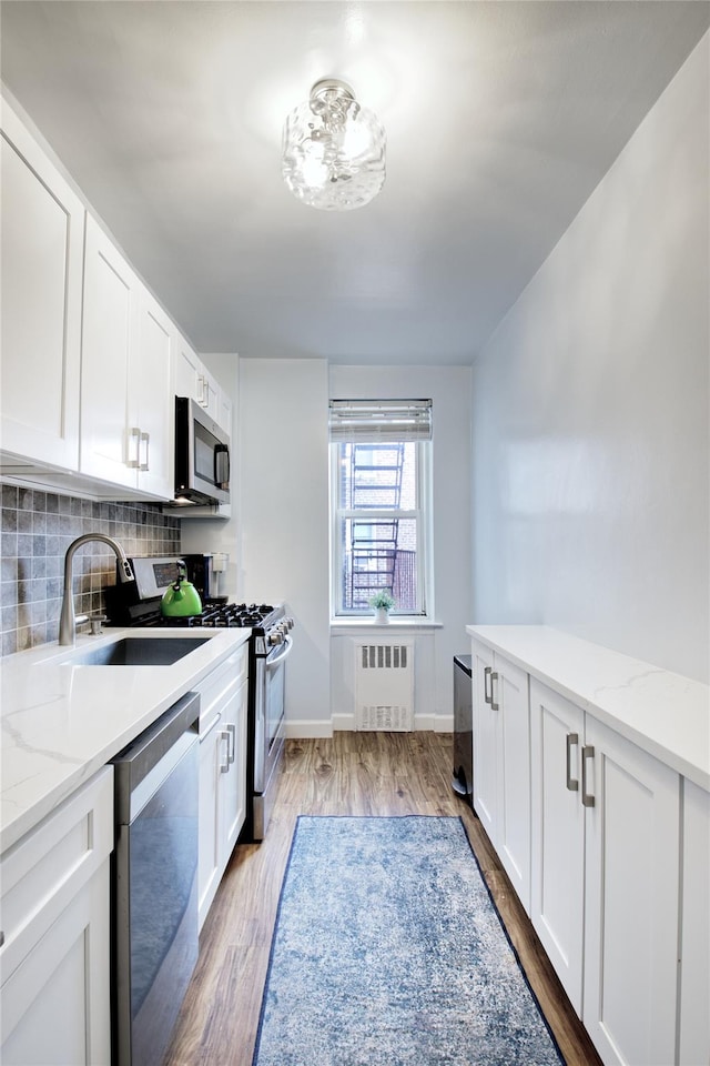 kitchen with white cabinets, appliances with stainless steel finishes, radiator heating unit, sink, and light wood-type flooring