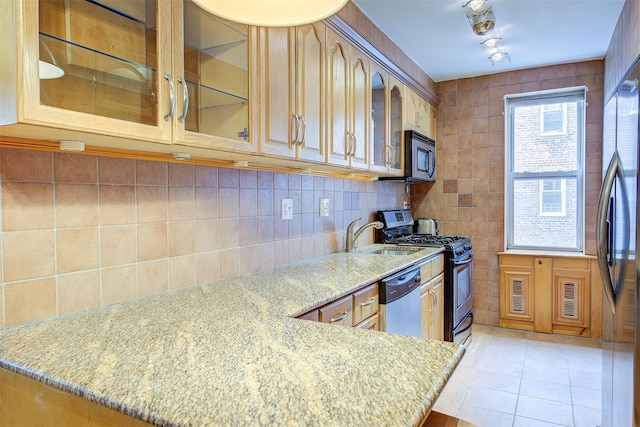 kitchen featuring a peninsula, a sink, appliances with stainless steel finishes, light stone countertops, and glass insert cabinets