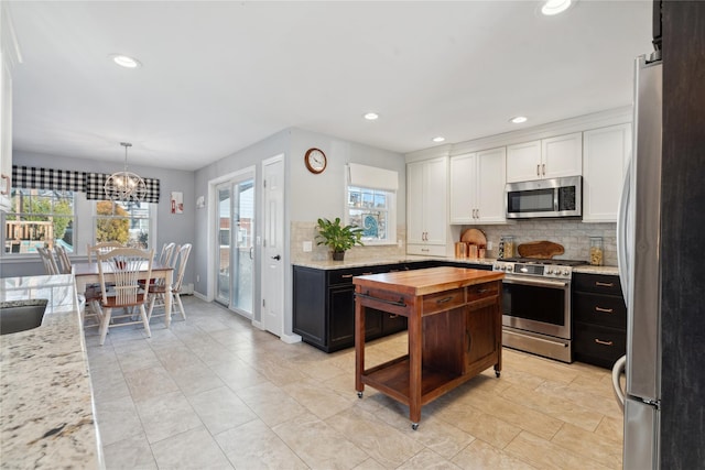 kitchen with pendant lighting, appliances with stainless steel finishes, white cabinetry, light stone countertops, and decorative backsplash