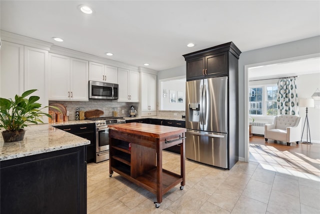 kitchen featuring tasteful backsplash, light stone counters, appliances with stainless steel finishes, radiator, and white cabinets