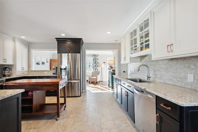 kitchen with sink, light stone counters, white cabinets, stainless steel appliances, and backsplash