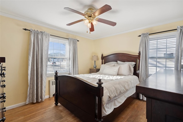 bedroom featuring multiple windows, hardwood / wood-style flooring, radiator heating unit, and ceiling fan