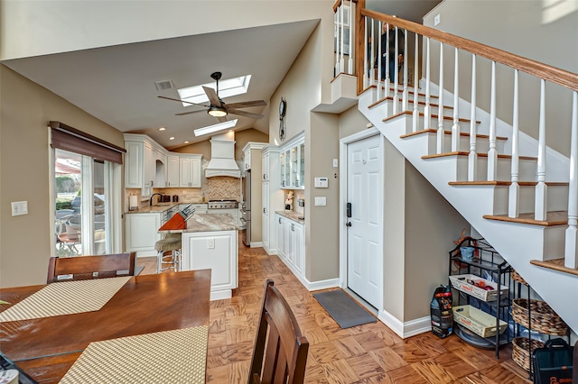 kitchen featuring premium range hood, white cabinetry, lofted ceiling with skylight, and light parquet floors