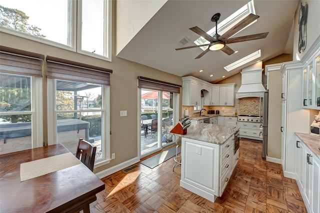 kitchen featuring premium range hood, light stone countertops, white cabinets, and a kitchen island