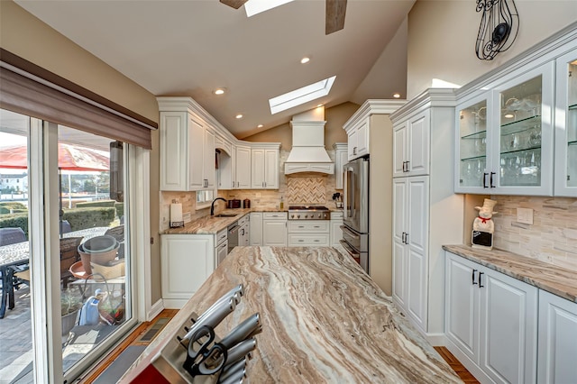 kitchen with appliances with stainless steel finishes, white cabinetry, sink, light stone countertops, and custom range hood