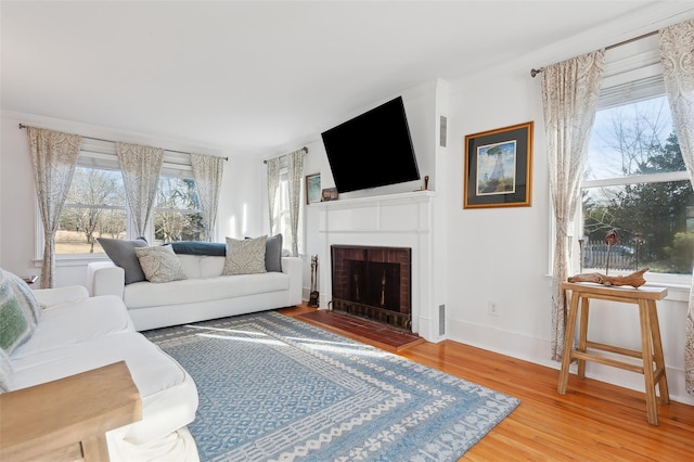 living room featuring a brick fireplace, wood-type flooring, and ornamental molding