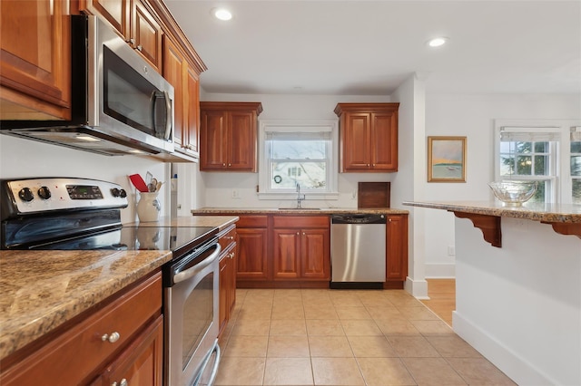 kitchen featuring sink, stainless steel appliances, light stone counters, and plenty of natural light