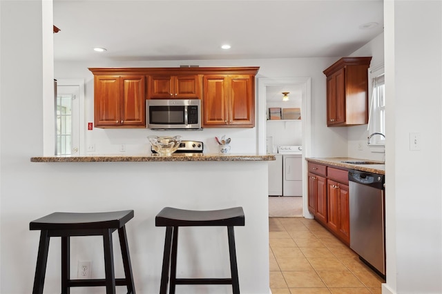 kitchen featuring sink, independent washer and dryer, light tile patterned floors, light stone counters, and stainless steel appliances