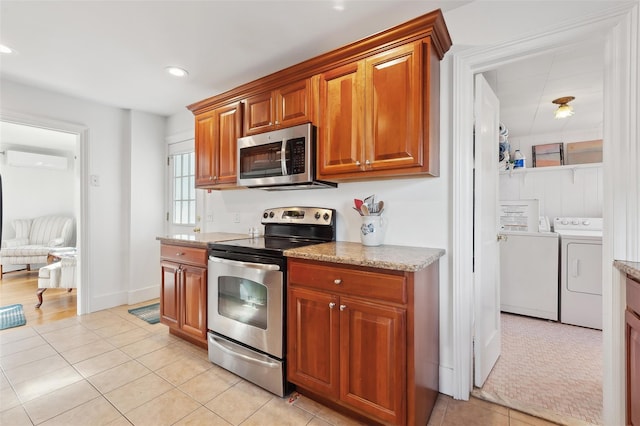 kitchen with appliances with stainless steel finishes, light tile patterned floors, washing machine and clothes dryer, light stone counters, and a wall mounted AC