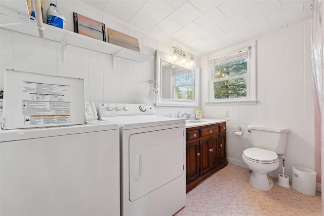 clothes washing area featuring sink, wood walls, and washing machine and dryer