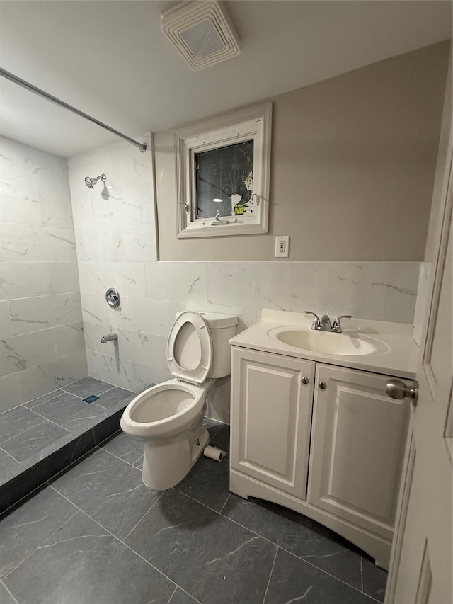 bathroom with vanity, tile walls, toilet, and tiled shower