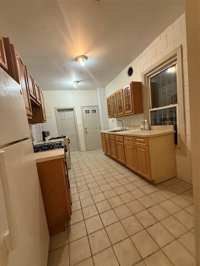 kitchen with sink, light tile patterned floors, stainless steel range with gas stovetop, white fridge, and decorative backsplash