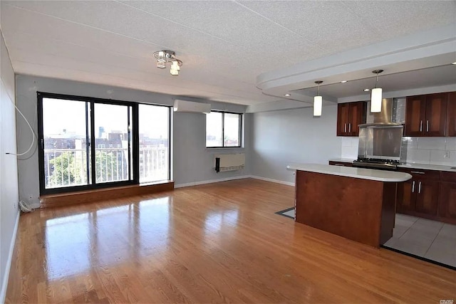 kitchen with a kitchen island, decorative light fixtures, tasteful backsplash, light wood-type flooring, and wall chimney exhaust hood