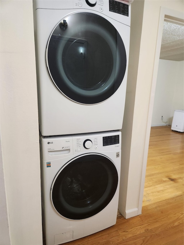 clothes washing area featuring hardwood / wood-style flooring, a textured ceiling, and stacked washer / dryer