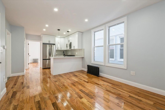 kitchen with pendant lighting, appliances with stainless steel finishes, radiator heating unit, white cabinetry, and kitchen peninsula